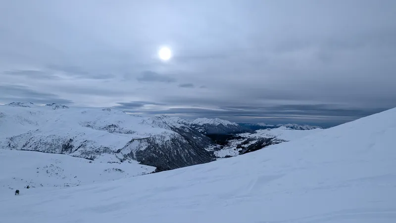Thick overcast sky over snowy mountains, sun barely visible