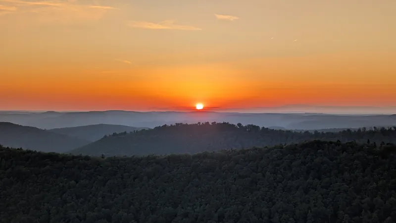 Hazy layered hills with an orange sun near the horizon